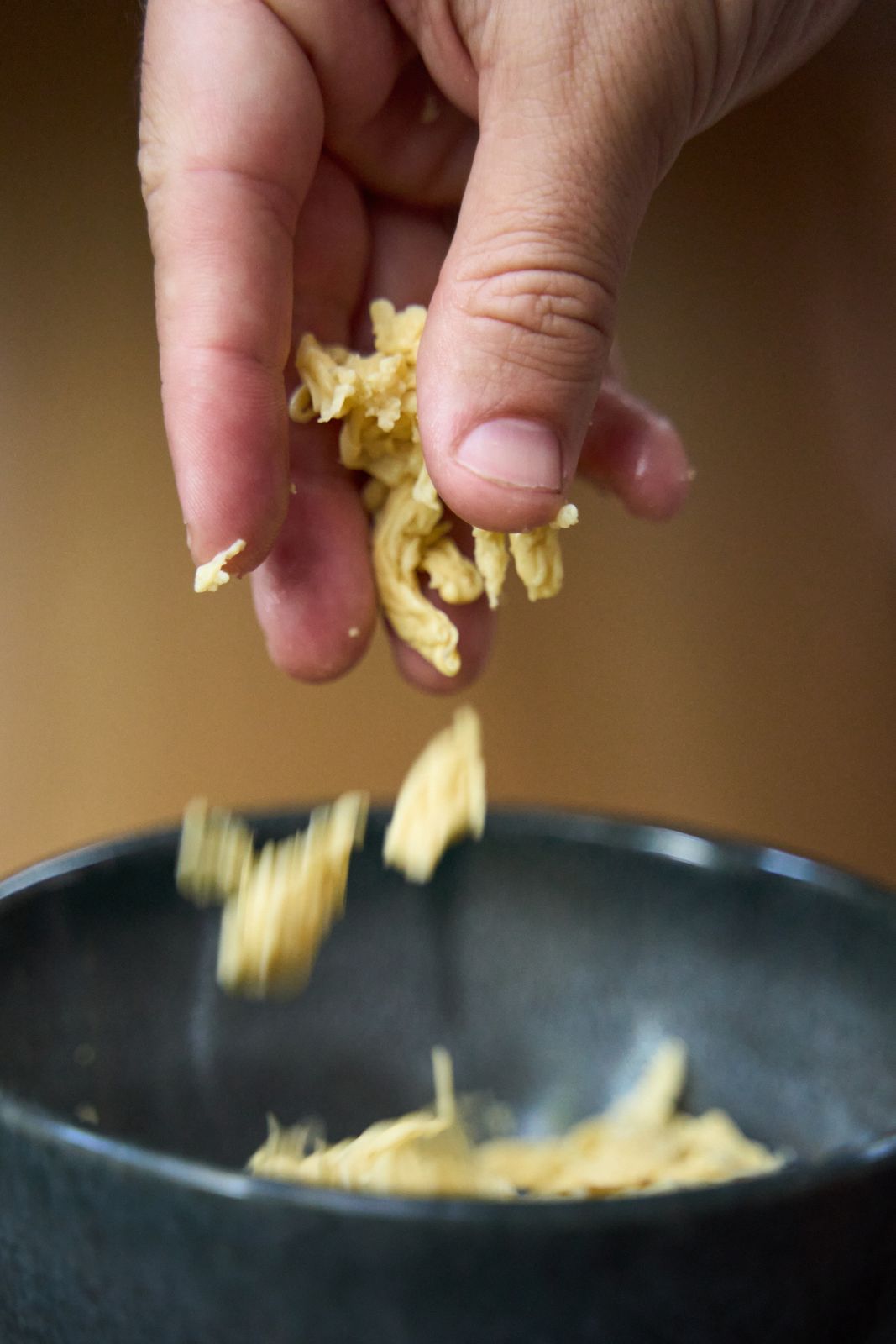 A hand dropping loose NoEgg Fibers into a dark bowl